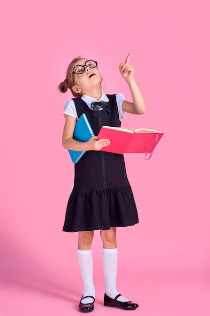 Preschool girl with glasses holding a book, raised her hand and finger up on a pink space