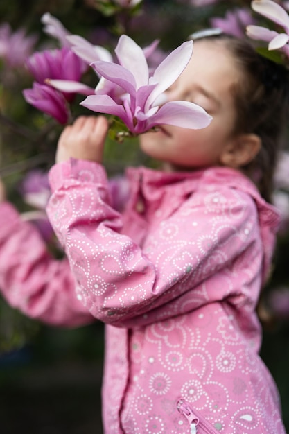 Preschooler girl in pink jacket enjoying nice spring day near magnolia blooming tree Springtime activities