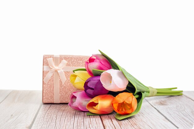 Present box and tulips on wooden rustic table with white background with space for text.