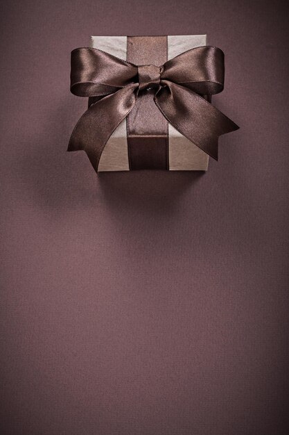 Present box with bow on brown background holidays concept