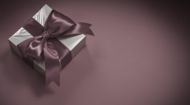 Present box with tied bow on red background holidays concept