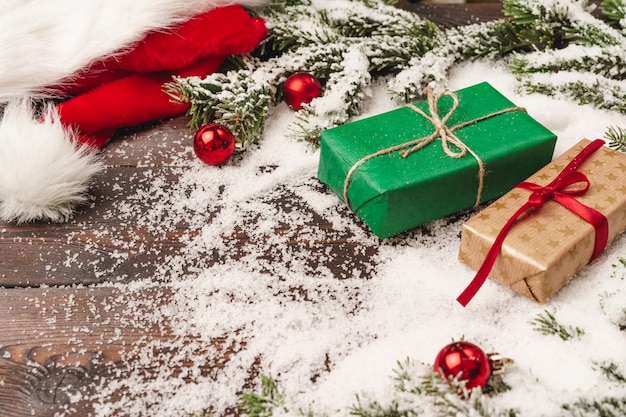 Presents on wooden background with fir tree branches and red baubles powdered with snow