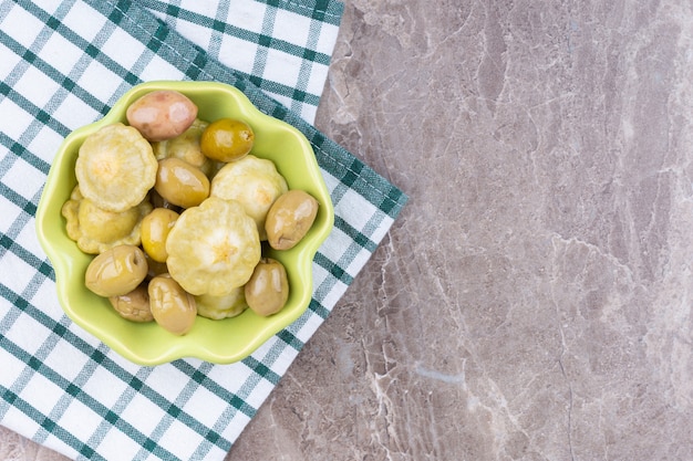 Preserved pattypan squash and olive in a bowl on a towel, on the marble.