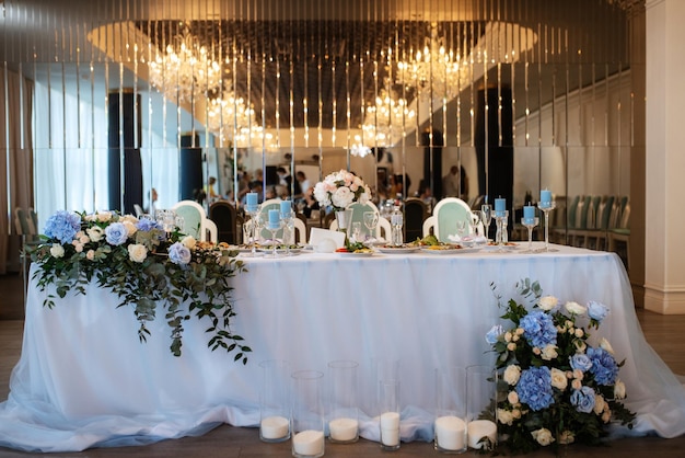 The presidium of the newlyweds in the banquet hall of the restaurant is decorated with candles and green plants, wisteria hangs from the ceiling