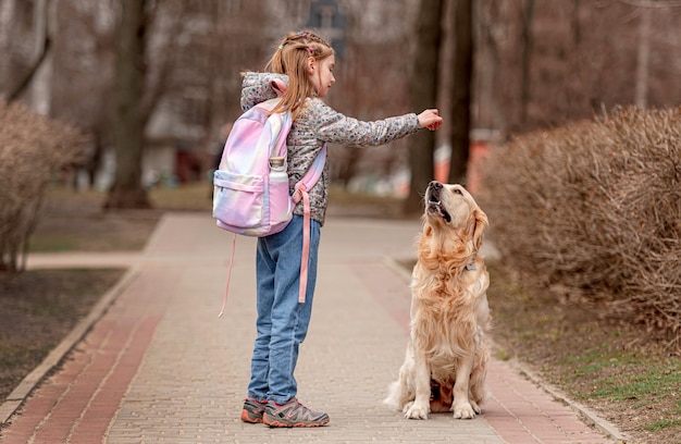 Preteen girl giving golden retriever dog yummy food on the nature