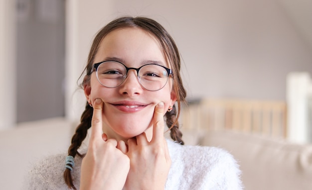 Preteen girl in glasses with pigtails making artificial smile, April fools day