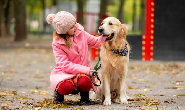 Preteen girl kid with golden retriever dog sitting in the park and petting doggy female child with p