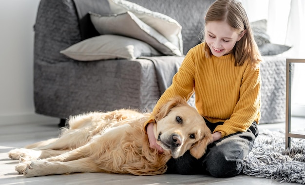 Preteen girl playing with golden retriever dog sitting on floor Pretty kid child petting doggy pet at home