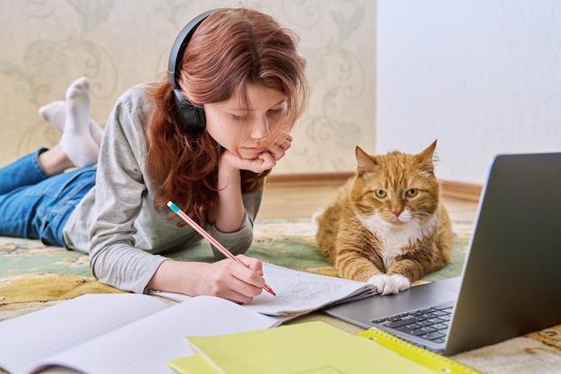 Preteen girl studying at home with ginger cat using laptop