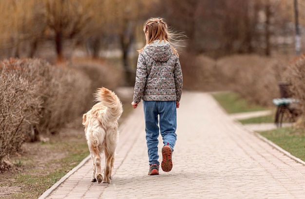 Preteen girl walking with golden retriever dog in the square in spring time