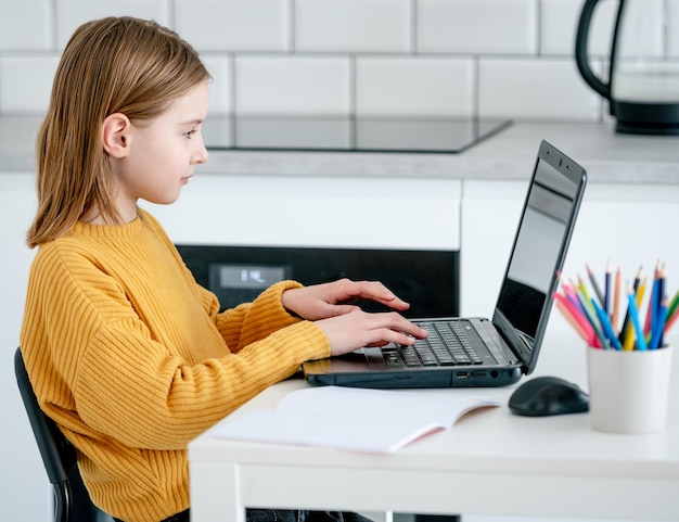 Preteen girl with laptop studying during remote lesson by internet Pretty schoolgirl learning with pc and having class online with new technologies at covid time