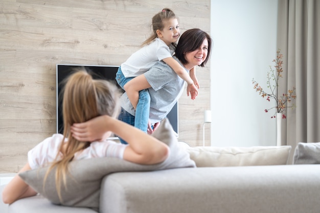 Preteen sad girl sitting on couch while mother having fun with younger sister, jealousy concept