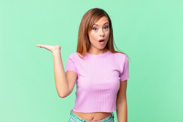 Pretty adult woman looking surprised and shocked, with jaw dropped holding an object