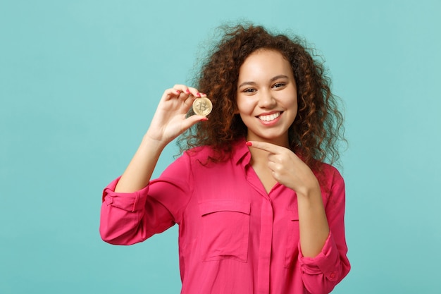 Pretty african girl in casual clothes pointing index finger on bitcoin future currency isolated on blue turquoise background in studio. People sincere emotions lifestyle concept. Mock up copy space.