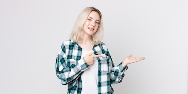 Pretty albino woman smiling, feeling happy, carefree and satisfied, pointing to concept or idea on copy space on the side