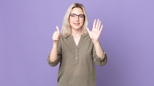 pretty albino woman smiling and looking friendly, showing number six or sixth with hand forward, counting down