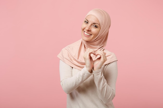 Pretty arabian muslim woman in hijab light clothes posing isolated on pink background. People religious Islam lifestyle concept. Mock up copy space. Showing shape heart with hands, heart-shape sign.