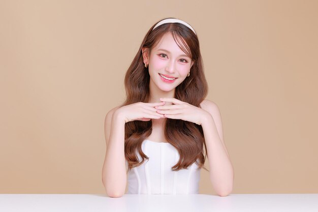 Pretty Asian beauty woman curly long hair with Korean makeup glowing face and healthy facial skin portrait smile on isolated beige background Cosmetology Plastic surgery