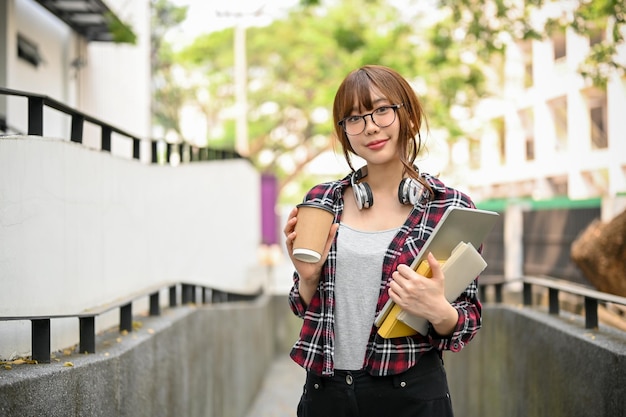 Pretty Asian female college student holding her stuff while walking outside of the campus building