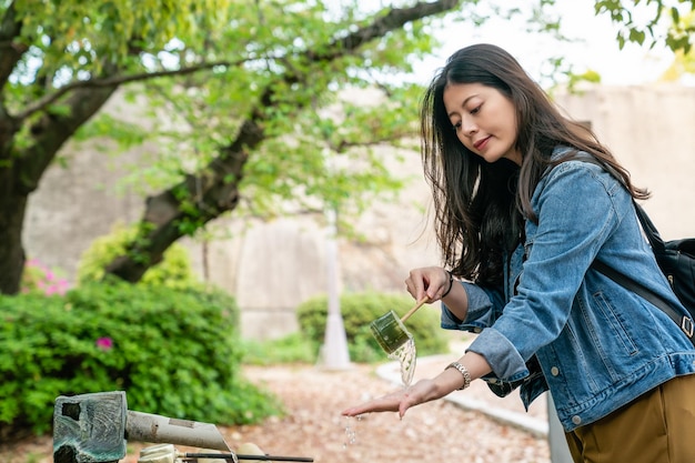 pretty asian girl smiling and taking bamboo ladle to wash her hand for a purifying ritual.