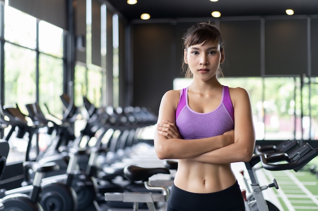 Pretty Asian girl with six packs in purple color sportswear standing and crossing arms in gym or fitness club.