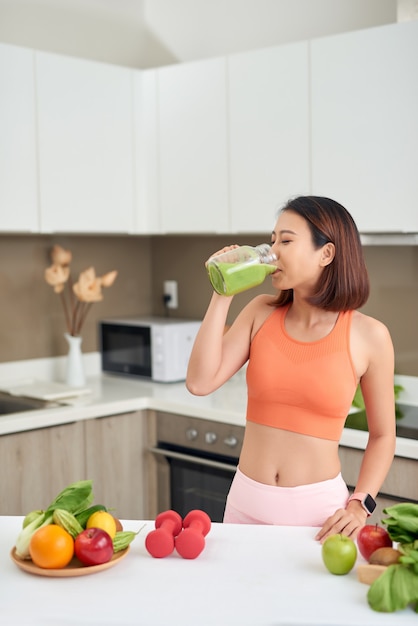 Pretty Asian woman drinking green detox juice while wearing sportive clothing