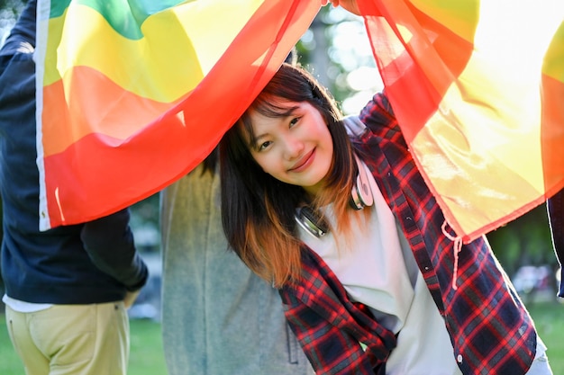 Pretty Asian woman holding LGBT rainbow flag with her friends in LGBT pride parade