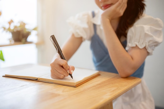 A pretty Asian woman is keeping diary listing her ideas while relaxing in a coffee shop