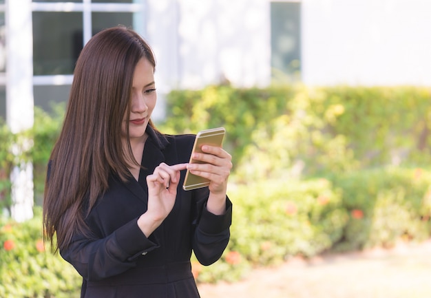 Pretty asian woman is texting on mobile in city park