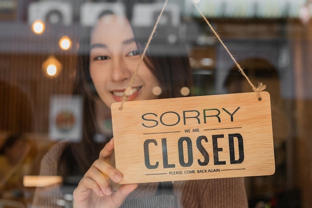 Pretty asian young owner retail coffee shop woman turning sign board to closed after finished work job and protection to pandemic of coronavirus Close store due to lockdown quarantine of covid