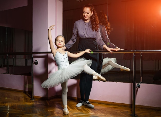 Pretty ballet teacher watching ballerina standing in nice pose during dance class A small girl and her instructor are engaged in choreography in the ballet school