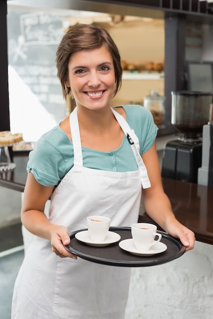 Pretty barista smiling at camera holding tray