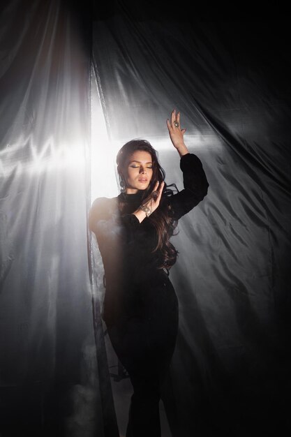 Pretty beautiful girl standing posing holding black curtains in her hands and playing with them Fashion studio portrait