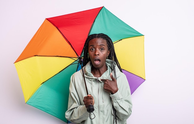 Pretty black woman looking shocked and surprised with mouth wide open, pointing to self. umbrella concept