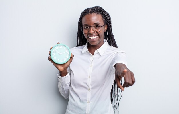 Pretty black woman pointing at camera choosing you. alarm clock concept