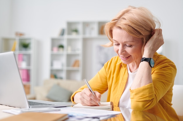 Pretty blond businesswoman in casualwear planning work or making notes while working remotely at home during self isolation