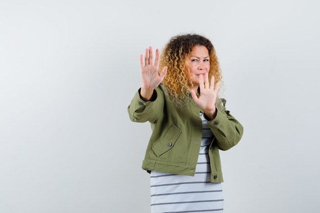 Pretty blond woman showing stop gesture in green jacket and looking disgusted , front view.