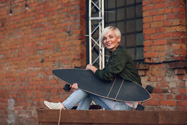 Pretty blond woman with longboard at  brick wall.