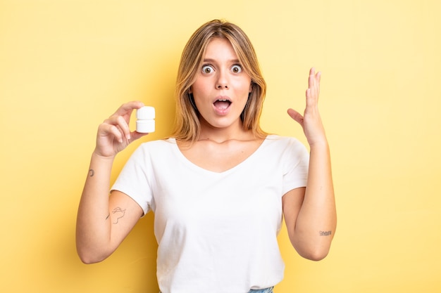 Photo pretty blonde girl feeling happy and astonished at something unbelievable. pills bottle concept