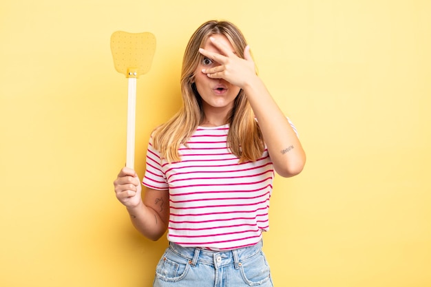 Pretty blonde girl looking shocked, scared or terrified, covering face with hand. kill flies concept