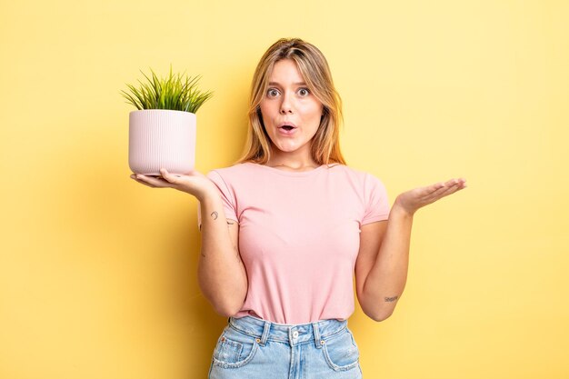 Pretty blonde girl looking surprised and shocked, with jaw dropped holding an object. houseplant concept