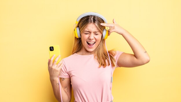 Pretty blonde girl looking unhappy and stressed, suicide gesture making gun sign. listening music concept