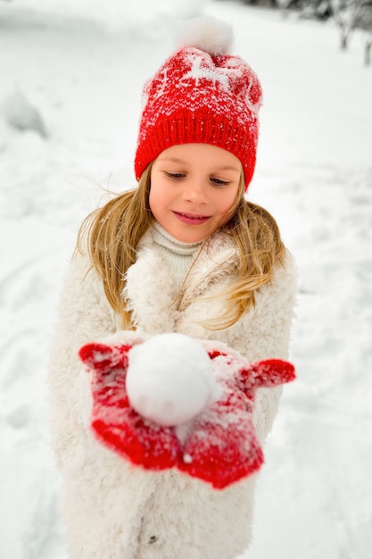 Pretty blonde girl in a red hat and knitted mittens plays with snow. winter portrait. winter fun