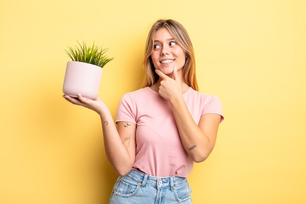 Pretty blonde girl smiling with a happy, confident expression with hand on chin. houseplant concept