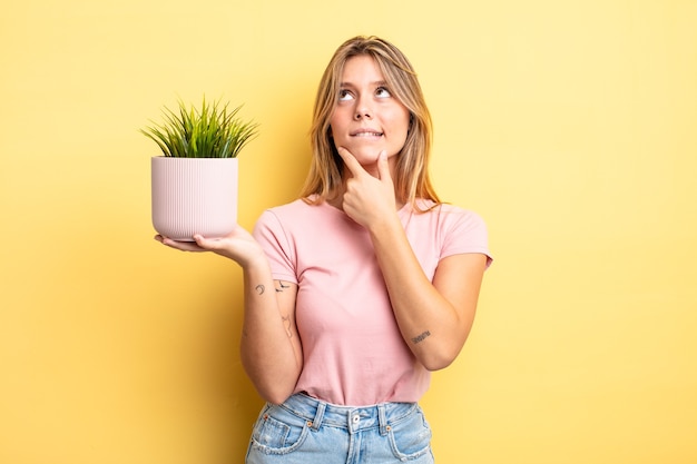 pretty blonde girl thinking, feeling doubtful and confused. houseplant concept