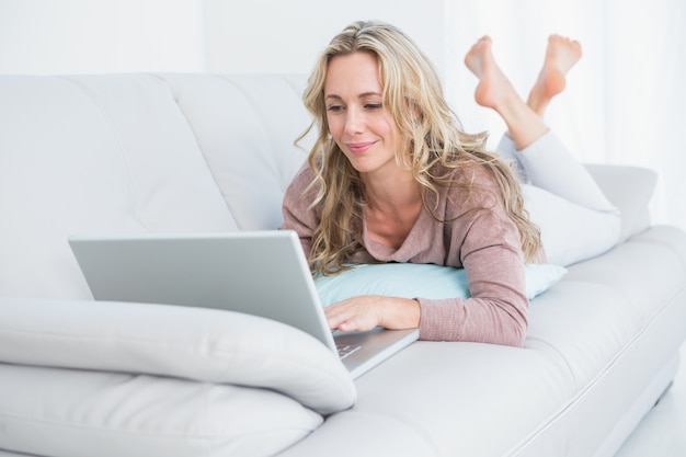 Pretty blonde lying on couch using laptop