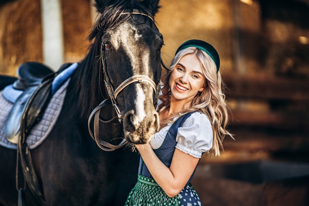 Pretty blonde in traditional dress  take care of big black horse at the farm