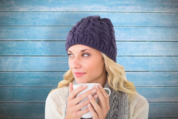 Pretty blonde in winter fashion holding mug against wooden planks