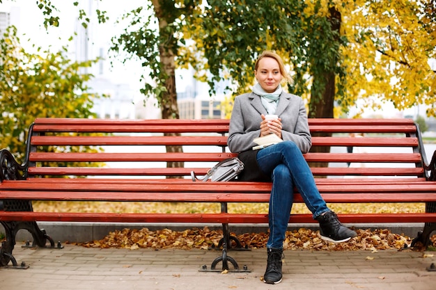 Pretty blonde woman sitting alone on a bench in autumn park