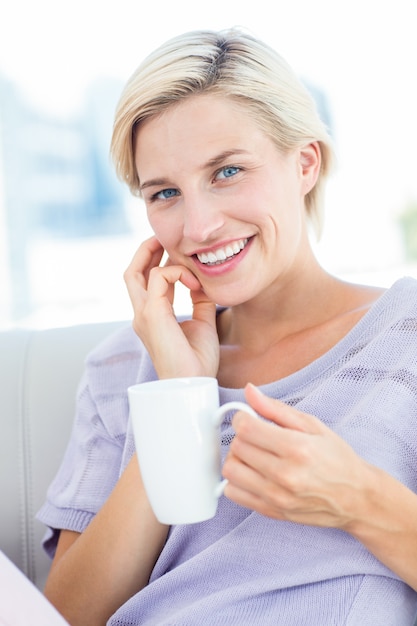 Pretty blonde woman sitting on the couch and holding a mug